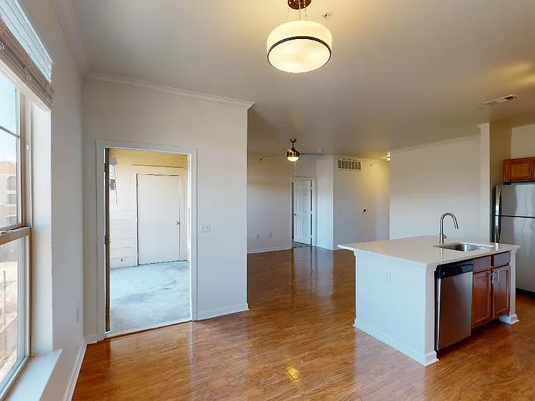 Apartment kitchen with stainless steel appliances, dining and living room with wood-style flooring.