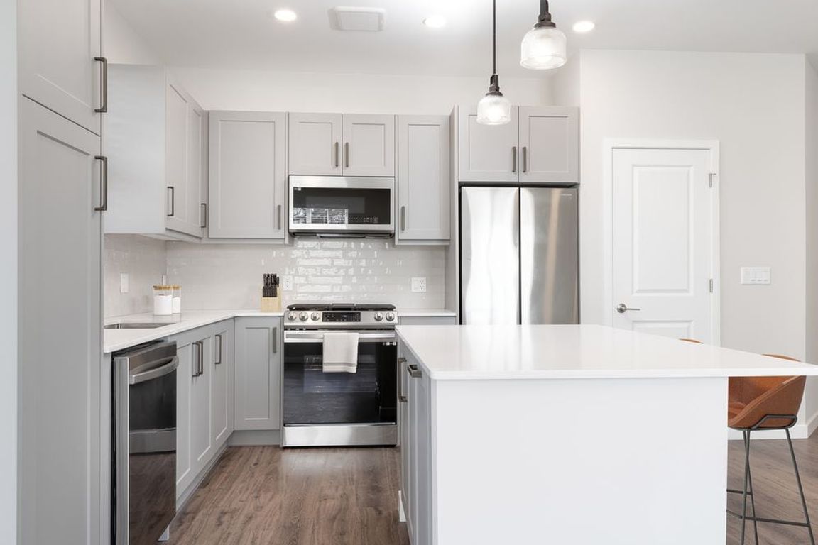 Modern kitchen with stainless steel appliances, white quartz countertop, light grey cabinetry, white tile backsplash, and hard surface flooring