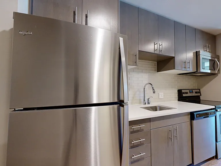 Apartment kitchen with stainless steel appliances, quartz countertops, and wood-style flooring.