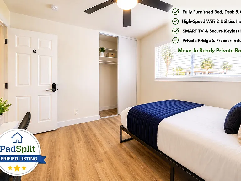 Private furnished bedroom with a full-size bed, desk setup, sliding-door closet, and a large window with blinds.