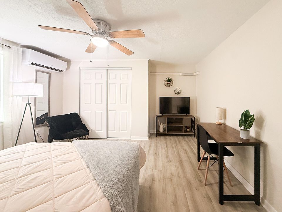 Well-laid-out bedroom with a ceiling fan, spacious closet, wall-mounted AC, and a dedicated desk area plus TV stand.
