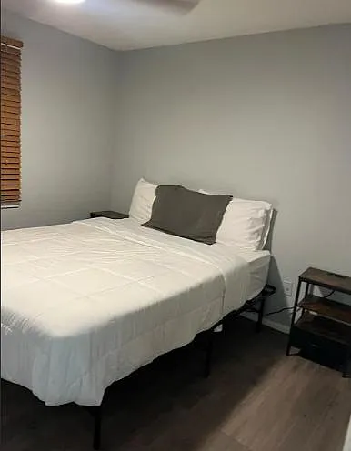 Neatly furnished bedroom featuring a full-size bed, neutral walls, wood-look flooring, and window blinds.