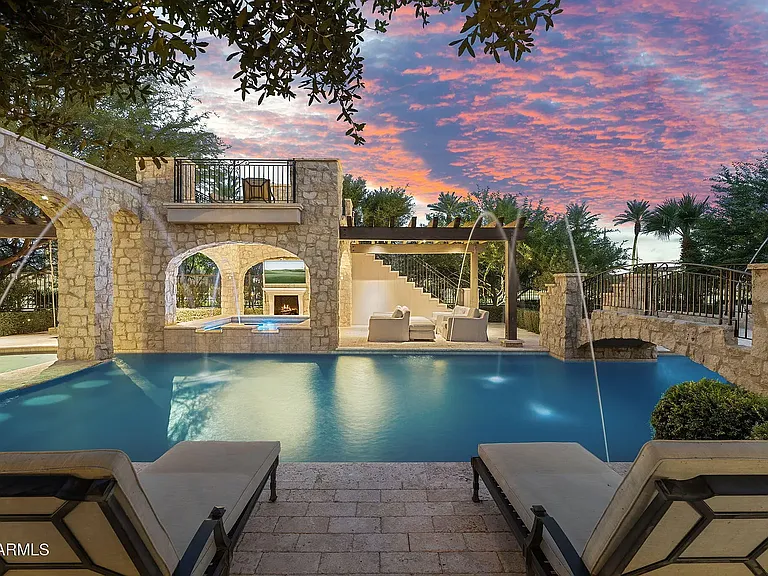 Dramatic sunset views enhance this luxurious pool retreat with cascading water features and sophisticated stone details