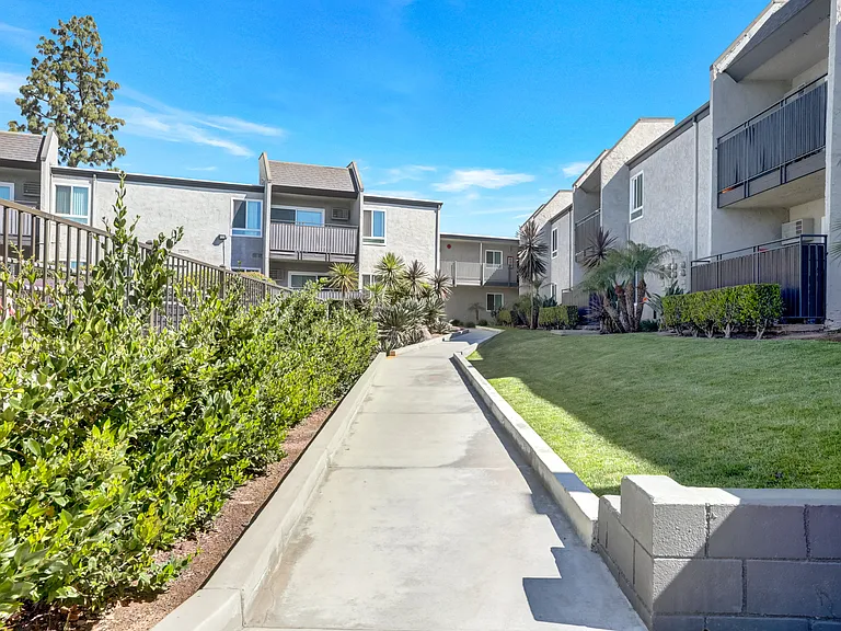 A concrete pathway leads through a well-manicured grassy area in front of apartment buildings.
