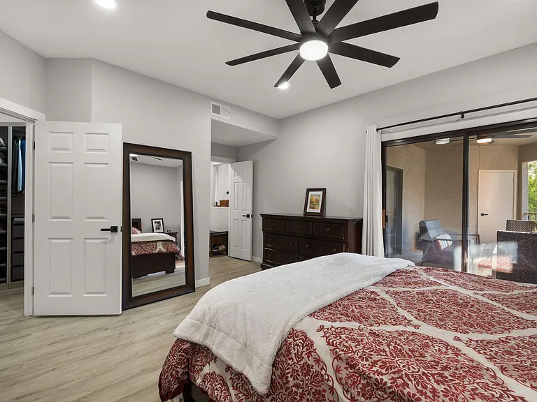 Spacious bedroom with ceiling fan, large mirror, dresser storage, and sliding doors to a private balcony; walk-in closet.