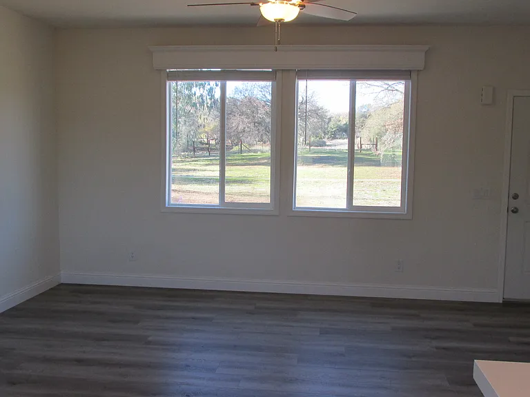 The living room area. Entry door is to the right of the windows. Ceiling fan with light included.