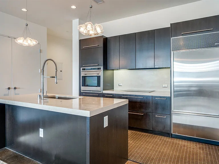 Kitchen with appliances with stainless steel finishes, decorative light fixtures, a kitchen island with sink, recessed lighting, and light stone countertops