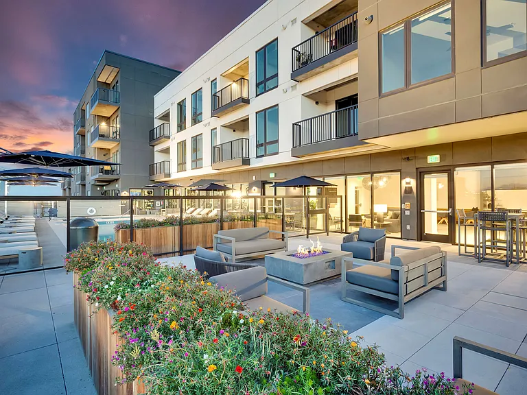 Luxurious apartment complex with modern outdoor seating and vibrant garden beds at sunset, showcasing elegant balconies and stunning architecture.