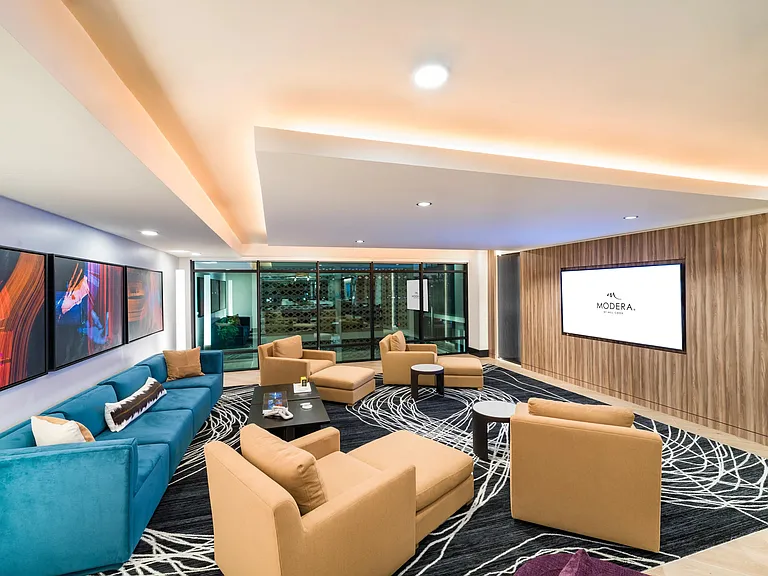 Bold colors and modern textures bring a vibrant energy to this clubroom featuring a media screen, perfect for casual hangouts or low-key movie nights.