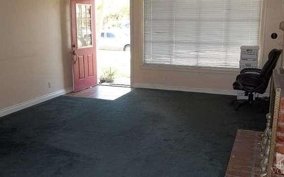 Living room has hole in E. wall, worn carpeting & original windows.