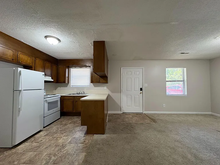 Open kitchen with ample wood cabinetry, breakfast bar, and full appliance set, flowing into a spacious adjacent living area.