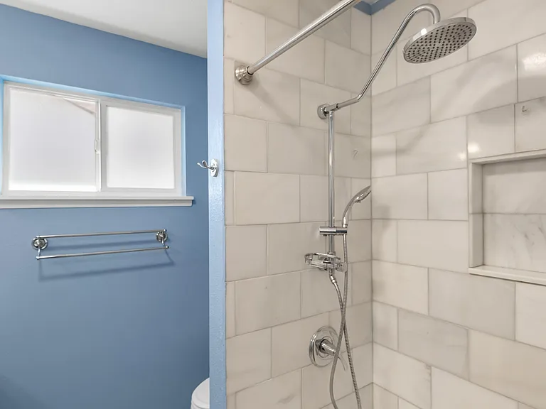 Updated tiled shower with rainfall showerhead, built-in niche shelving, and a frosted window for privacy and light.