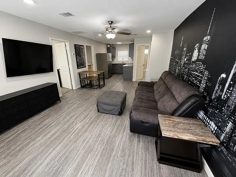 Open living area with oversized sectional, wall-mounted TV, and adjacent eat-in nook leading into the kitchen.