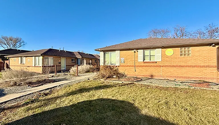 Charming brick apartment exterior with a landscaped front yard under a clear blue sky.