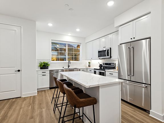 A modern, well-lit kitchen with white cabinets, stainless steel appliances, and a marble-topped isla