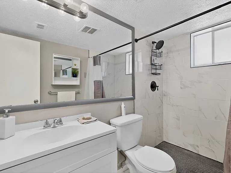 A clean bathroom featuring a shower, toilet, and vanity, with neutral-colored tiles and bright lighting.