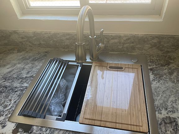 Kitchen workstation has bamboo cutting board, stainless steel colander, dish drying roll up rack and bottom grid
