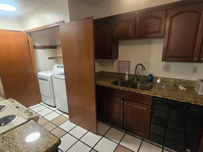 Compact kitchen with granite-look counters, double-basin sink, ample cabinetry, and an adjacent in-unit laundry nook.