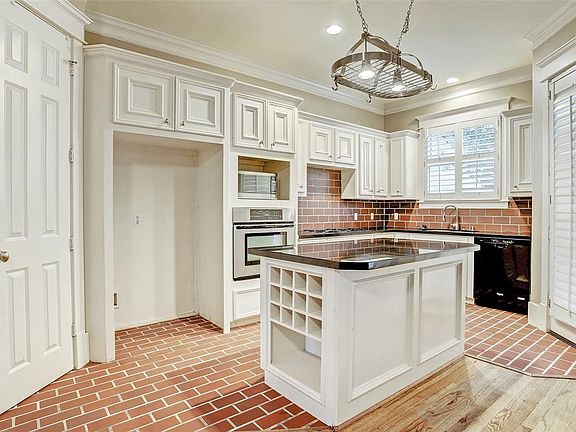 Kitchen has decorative tile floor and backsplash, white custom cabinets, kitchen island with wine rack, and granite counters.