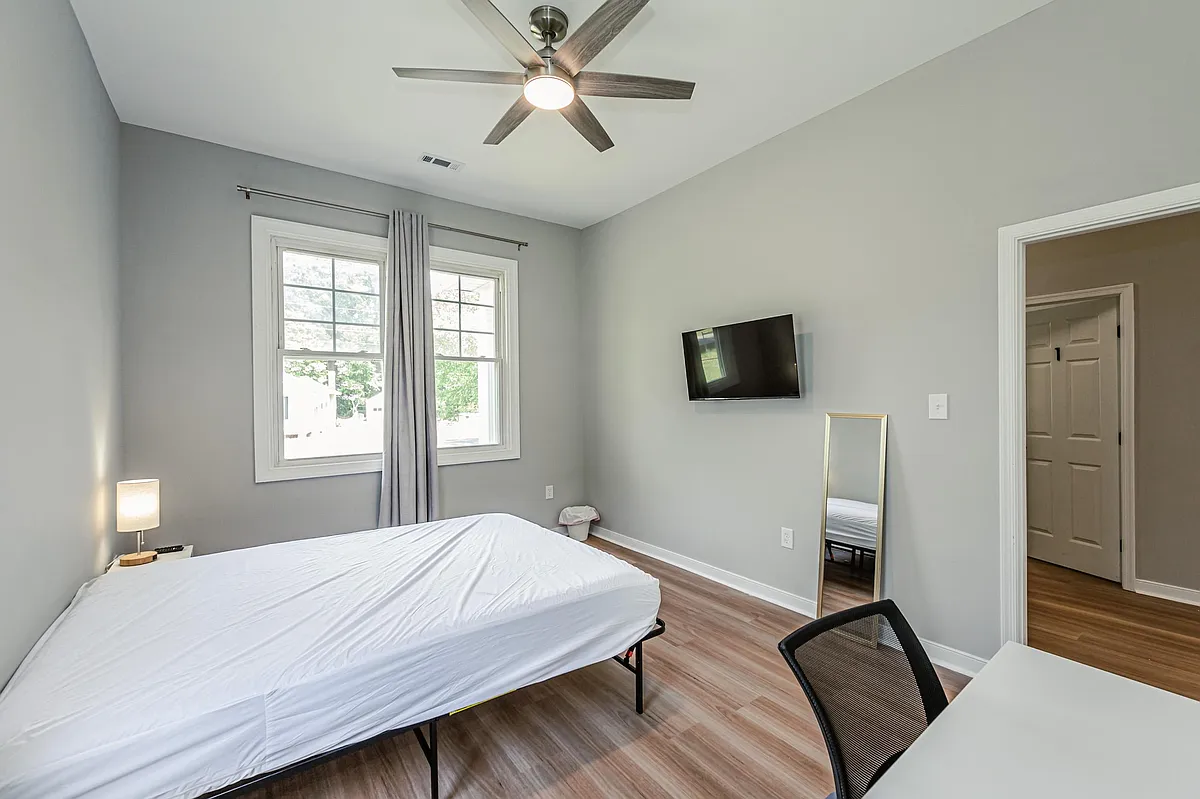 Spacious bedroom with large window, ceiling fan, wall-mounted TV, and room for a bed plus a small desk setup. - Greenwood Rd