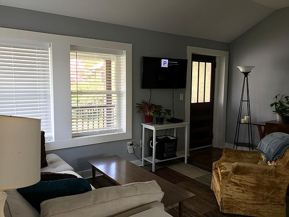Living room. West Elm couch, wall mount smart TV, West Elm table. Door opens to long porch overlooking driveway.