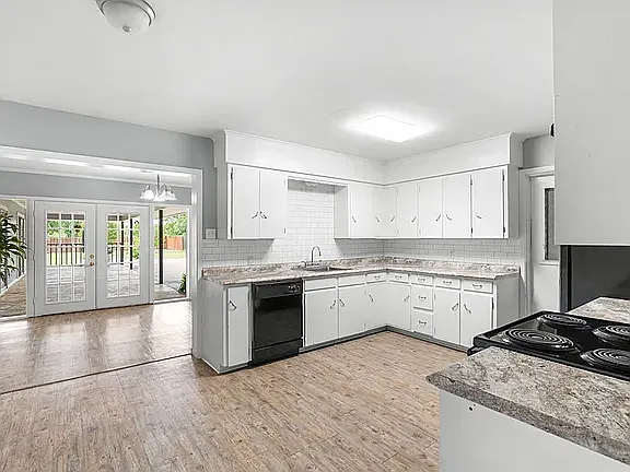 Roomy Kitchen with black appliances, generous countertops, and view of Dining Rrea with 15-pane glass French doors opening to outside patio for entertaining; black refrigerator on range wall with door leading to garage at end of sink cabinets