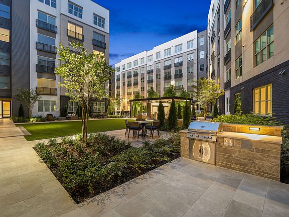 Charming urban courtyard with modern apartment views, featuring lush landscaping, a sleek outdoor grill, and cozy seating under a pergola.