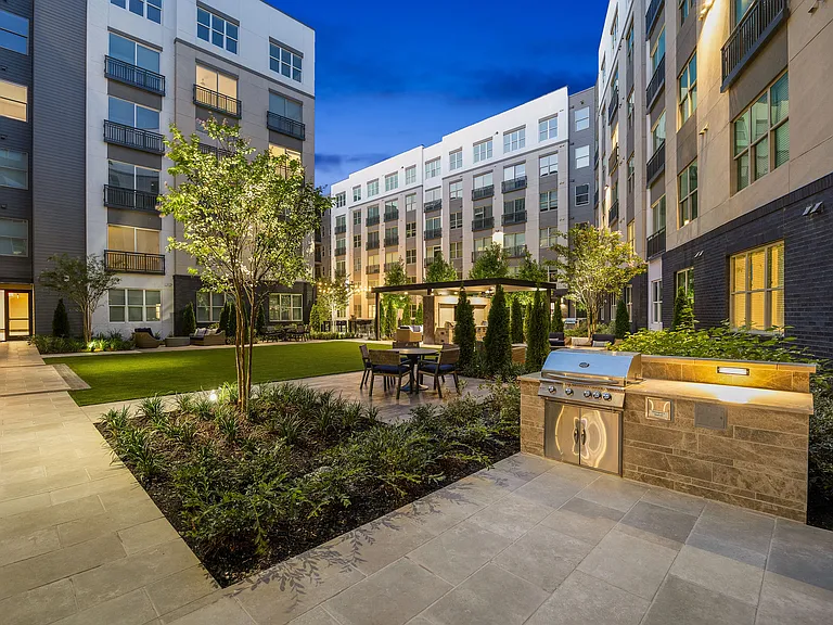 Charming urban courtyard with modern apartment views, featuring lush landscaping, a sleek outdoor grill, and cozy seating under a pergola.