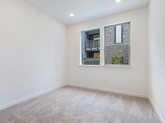 A bright, empty room with a large window overlooking a brick exterior wall, featuring a hardwood flo