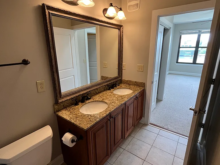 A luxurious condo bathroom with polished granite countertops and dual sinks, combining sleek design with everyday functionality. A frameless glass shower creates an open, refined feel, accented by a distinctive rainfall shower head. Stunning river view.