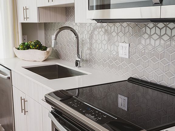 Beautiful tile backsplash in kitchen with sleek glass stovetop and large farmhouse sink