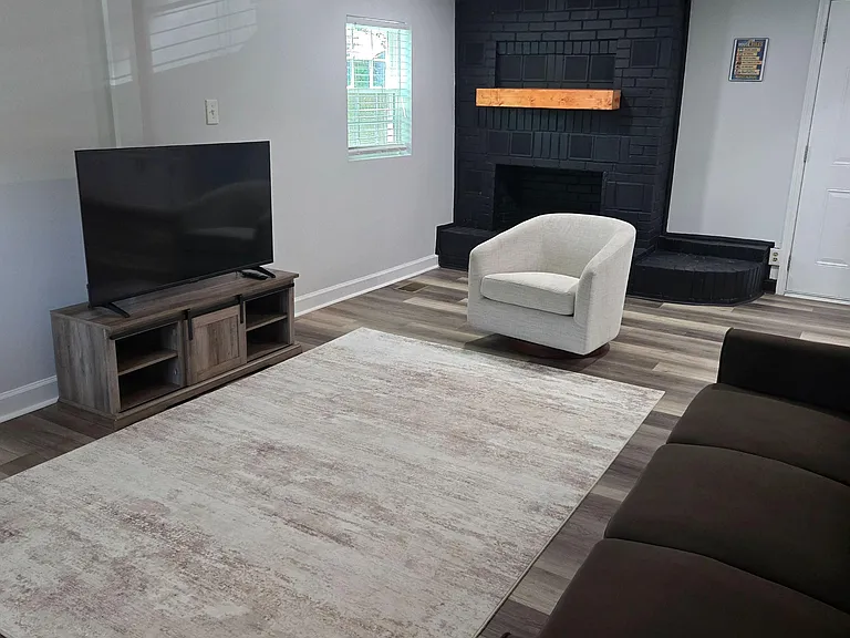 Living area with large rug, TV setup, and a statement brick fireplaceideal for relaxing or shared hangouts.
