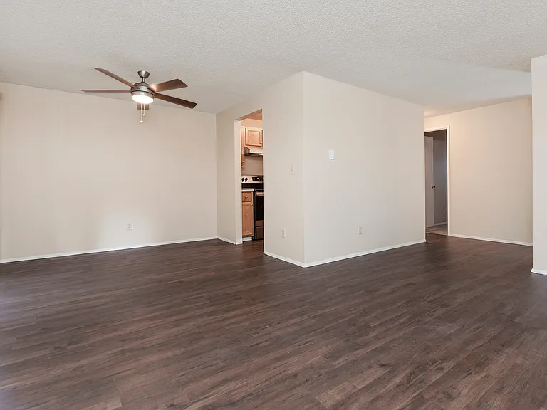 Open-concept living area with dark wood floors, neutral walls, and a modern ceiling fan, leading into the kitchen. Open-concept living area with dark wood floors, neutral walls, and a modern ceiling fan, leading into the kitchen.