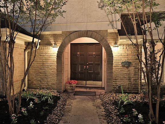 DOUBLE SOLID WOOD FRONT DOORS - A close up image of the recently painted double doors and arched brick entry. The home provides a balanced symmetry with crepe myrtles on each side, a pathway of bull rock and lighted sconces. This English style home b