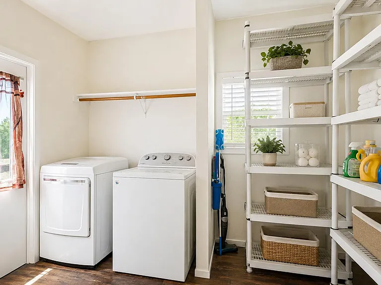 Dedicated laundry area with full-size washer/dryer, open shelving for supplies and linens, and a window for airflow.