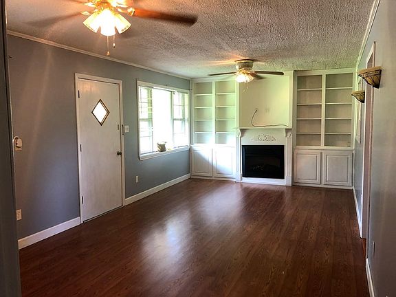 Spacious open living area with large window, fireplace, and built in bookcases and storage. Flows into kitchen and eating nook.