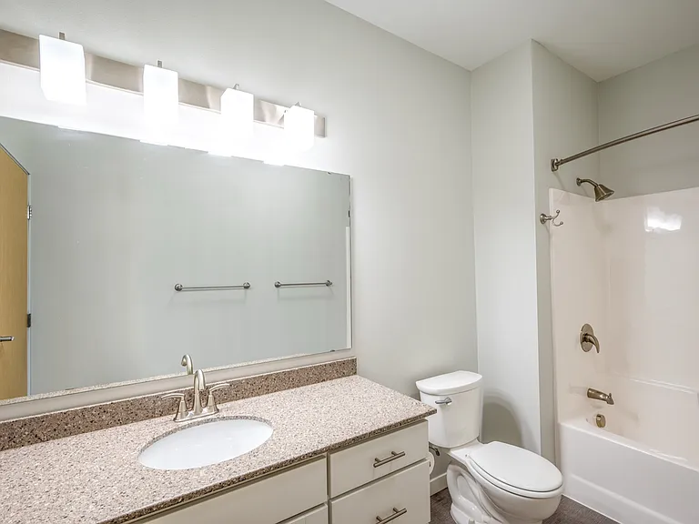 Modern bathroom with sleek countertop, large mirror, and elegant lighting. Features a bathtub and contemporary fixtures, creating a bright and inviting space. Modern bathroom with sleek countertop, large mirror, and elegant lighting. Features a bathtub an