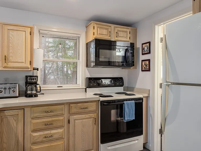 Kitchen. Refrigerator, electric stove and oven, microwave, coffee maker, toaster, and full plates, bowls, glasses, mugs, forks, knives, spoons, pots and pans, and kitchen utensils.