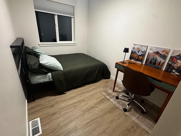 Small and cozy private furnished bedroom with a full-size bed, work desk, and window with shade.