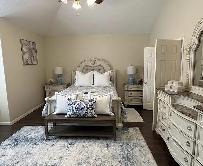 Spacious bedroom with a queen bed, matching nightstands, ceiling fan light, and dresser with mirror on hardwood floors.