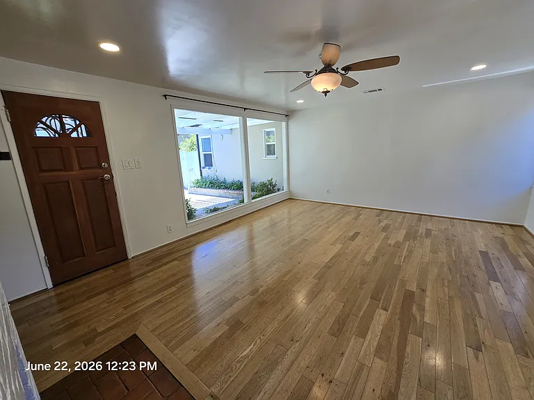 Family size living room with brick (non fire burning fireplace) wood floors, smooth ceilings, remote ceiling fan forced air and heat