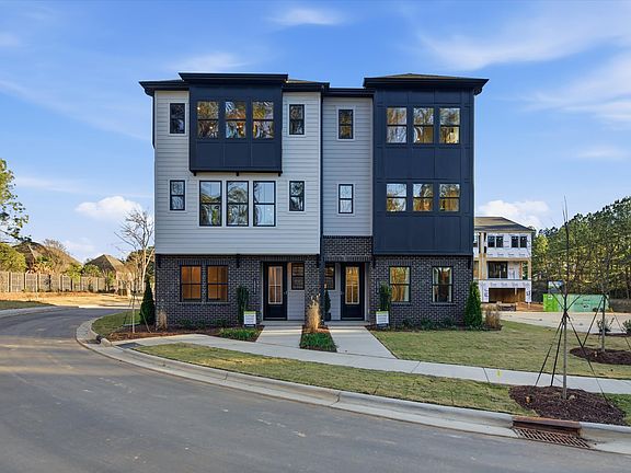 A modern, multi-story townhouse complex with a gray exterior, surrounded by a grassy lawn and trees