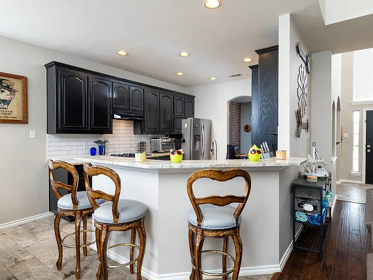 Bright kitchen with black cabinets, stainless appliances, and a curved breakfast bar with seating. Perfect for cooking, gathering, and enjoying meals together.