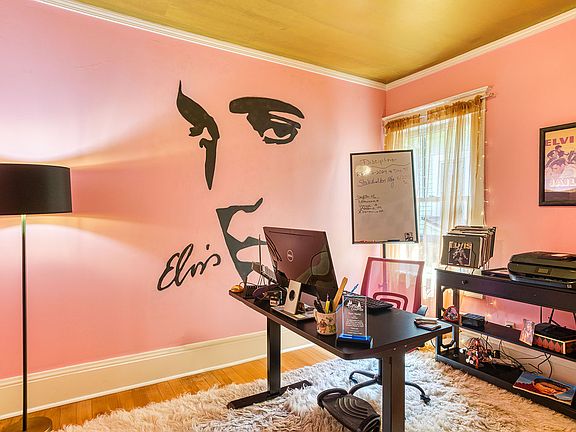 Step into a retro-inspired office with 1950s pink walls, a gold ceiling, and sheer gold curtains adorned with soft lights. A bold and iconic large profile of Elvis' face serves as the centerpiece, infusing the room with undeniable character.