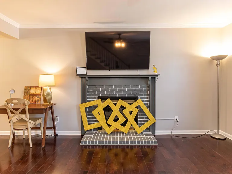 Shared living area with a brick fireplace, mounted TV, and hardwood floors, plus a small desk nook for work or study.