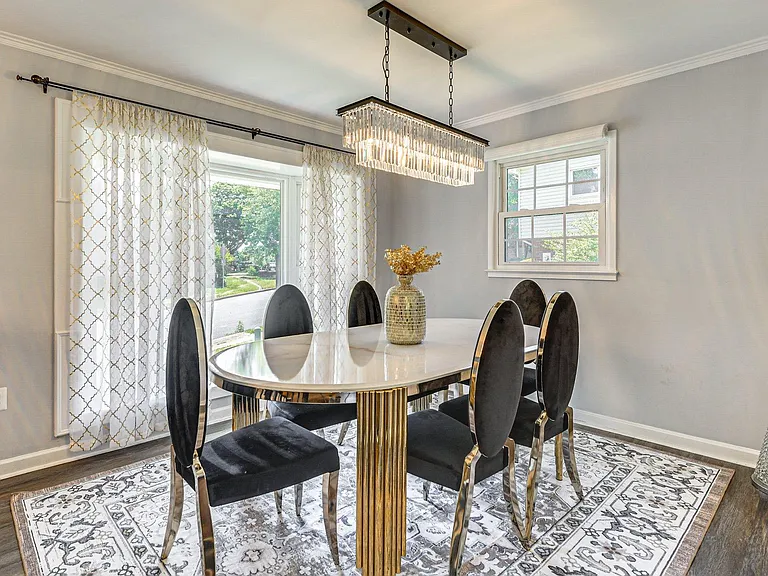 Dining area with an oval table for six, statement chandelier, and large windows with curtains for natural light.