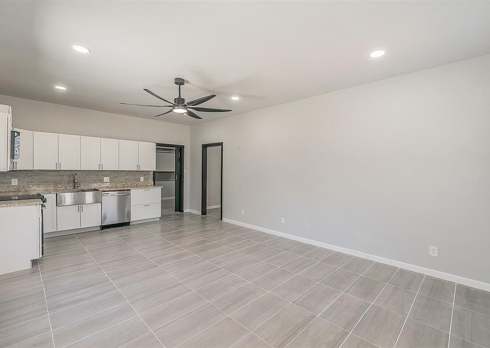 Kitchen featuring white cabinetry, stainless steel dishwasher, backsplash, a sink, and ceiling fan