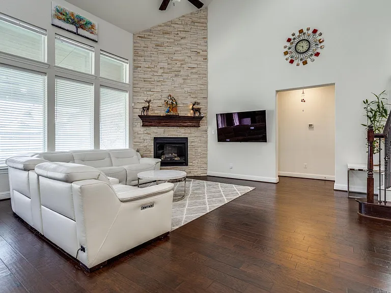Living room with a stone fireplace, high vaulted ceiling, ceiling fan, and dark hardwood / wood-style floors
