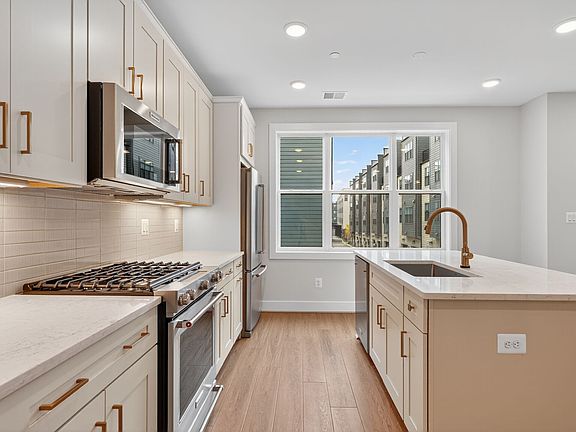 A modern, well-lit kitchen with white cabinets, stainless steel appliances, and a large window overl