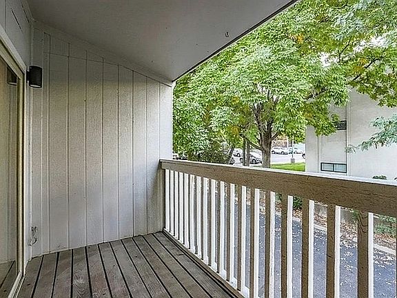 Charming apartment balcony with wooden decking and tranquil views of lush green trees, perfect for serene outdoor relaxation.